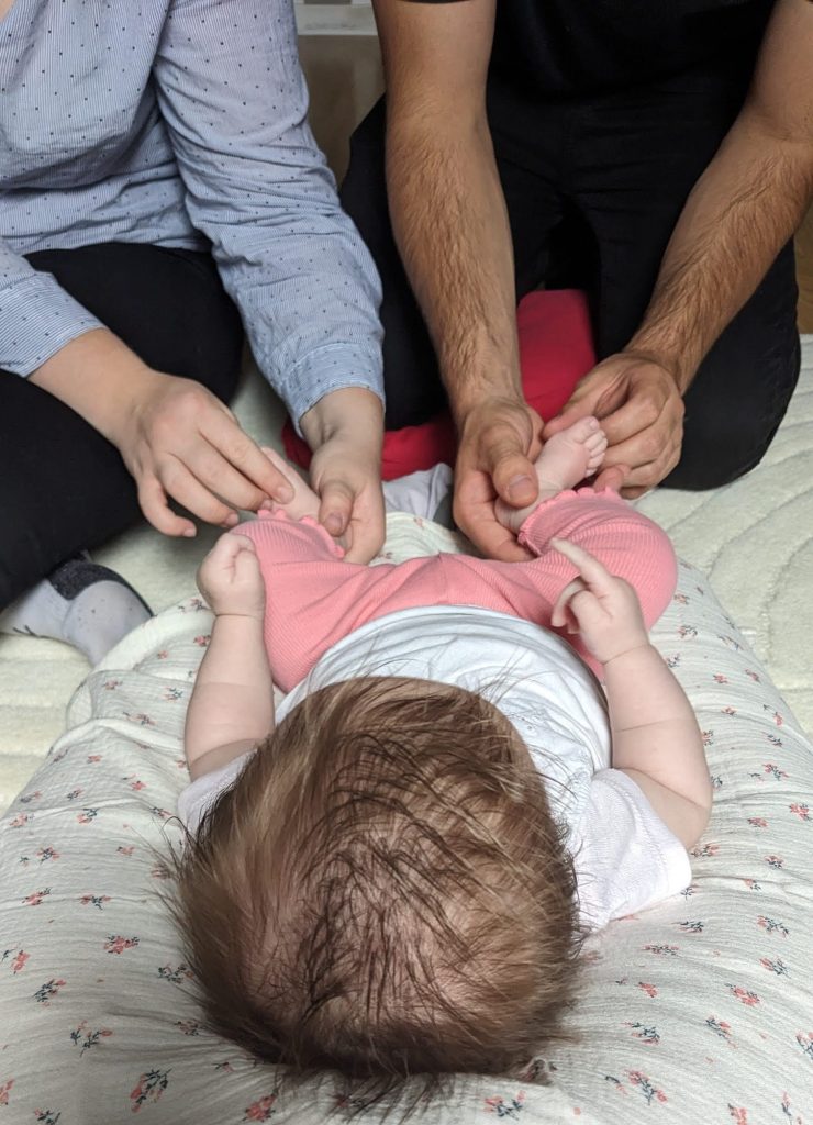 Deux parents posent les mains sur les pieds de leur bébé allongé, pendant un atelier de réflexologie