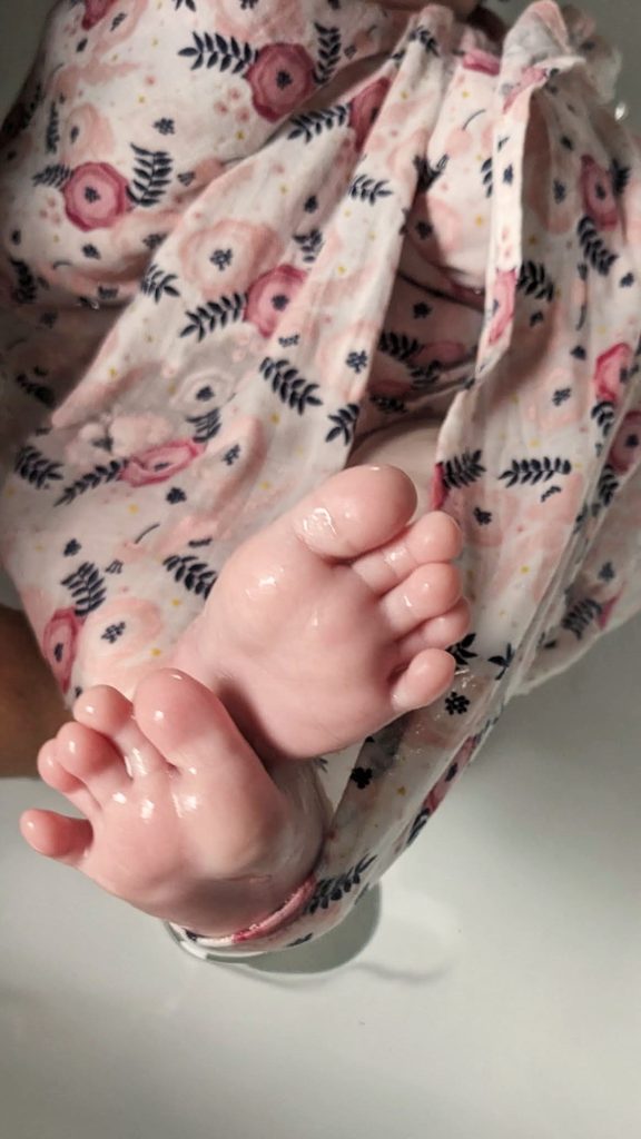Pieds d’un bébé dépassant d’un lange fleuri pendant un bain enveloppé