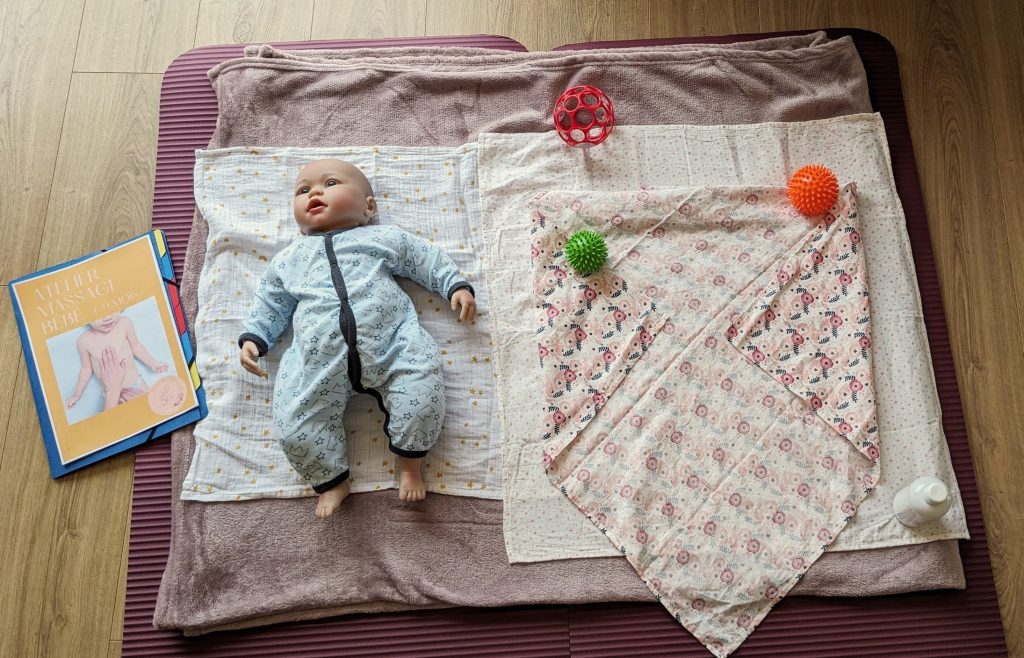 Installation de l’atelier massage bébé : poupon sur un tapis, livret, linges et balles sensorielles