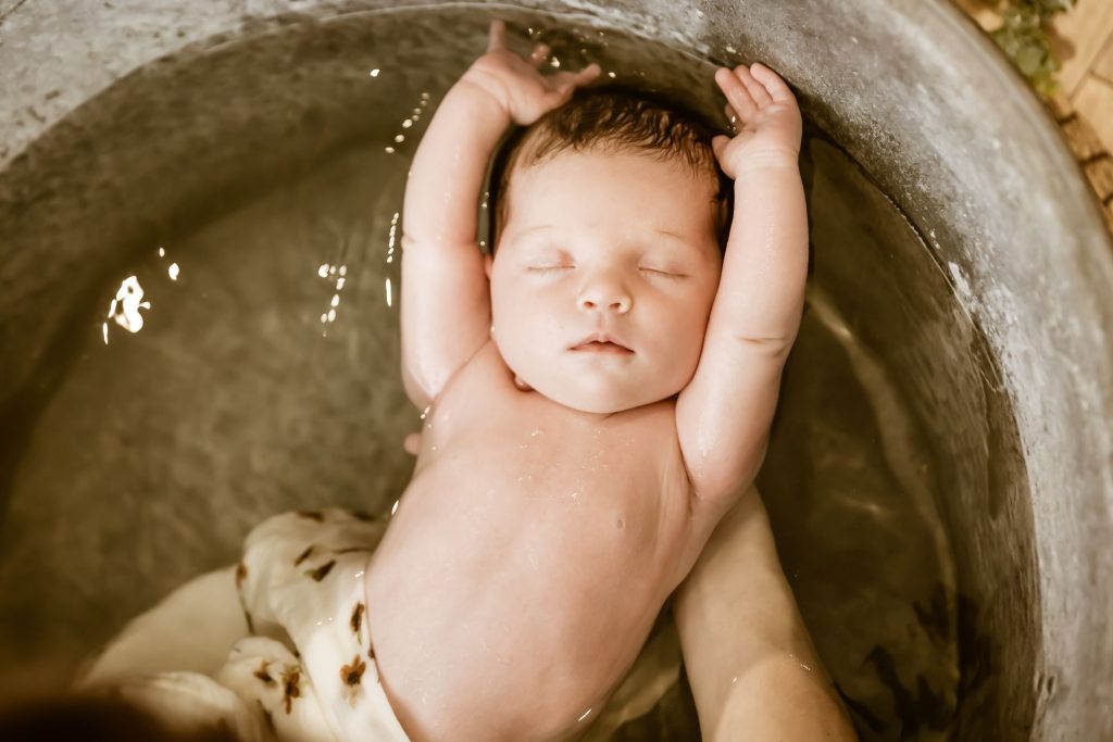 Nouveau-né endormi dans son bain, les bras au-dessus de la tête, lors d’un bain enveloppé photographié
