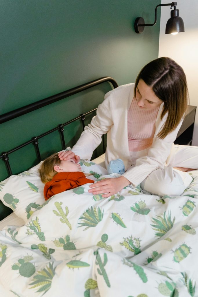 Une mère veille son enfant malade couché dans son lit, la main sur son front